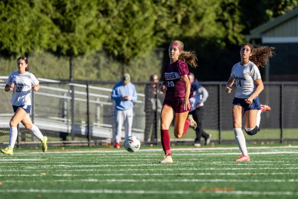 TRS vs Freehold Twp - Shore Sports Insider Toms River South junior Emma Turnbach. (Photo: Doug Phillips) - TRS vs Freehold Twp' soccer match: three players sprint toward the ball on a fenced turf field, two in white and one in maroon.
